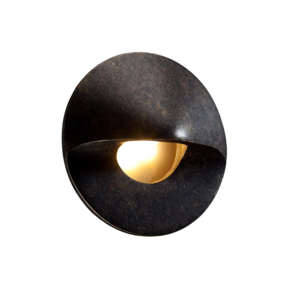 FX MO round hardscape LED wall light in antique tumbled finish, illuminated at night on stone surface, illustrating warm glow and recessed-style effect.