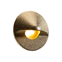FX MO hardscape LED wall light in natural brass finish, studio product shot showing round faceplate, interchangeable faceplate detail, and frosted diffuser.