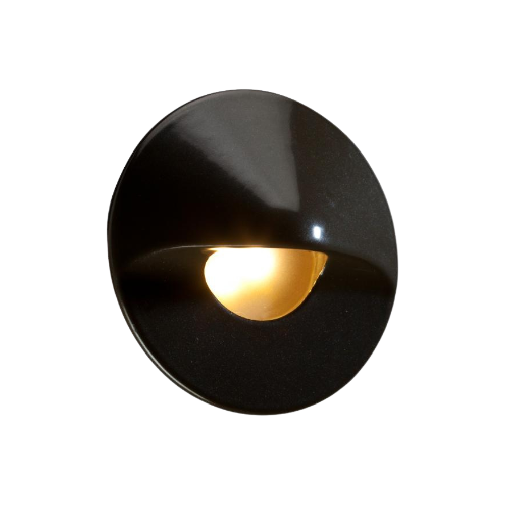Close view of FX MO round hardscape LED wall light in bronze metallic finish, illuminated, showing frosted lens and 3-LED aperture.