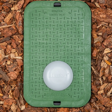 Illustration of Hunter Wireless Valve Link mounted on valve box lid with antenna and nearby irrigation valves, demonstrating wireless connectivity and placement (approx. 100 characters).