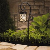 Angled view of Kichler Almeria 15426BKT 12V path and spread light in textured black highlighting the lamp head, amber-tinted glass, and mounting stake (product photo).