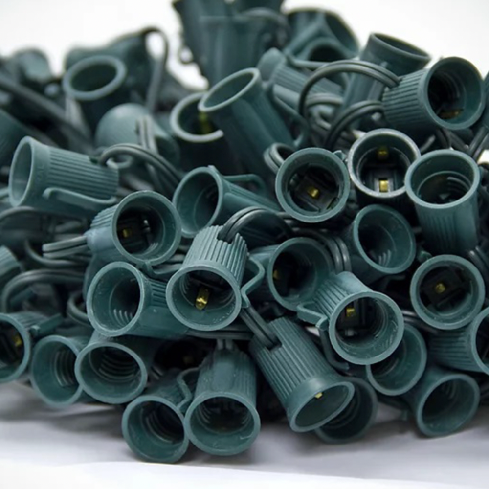 Photograph of Seasonal Source green C7 socket wire spool, 100 ft SPT-1 cord with 100 C7 (E12) sockets and male plug visible.